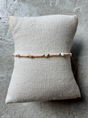 Armbånd med lyserøde og gyldne perler på en beige pude, fremhæver perlernes farver og design.