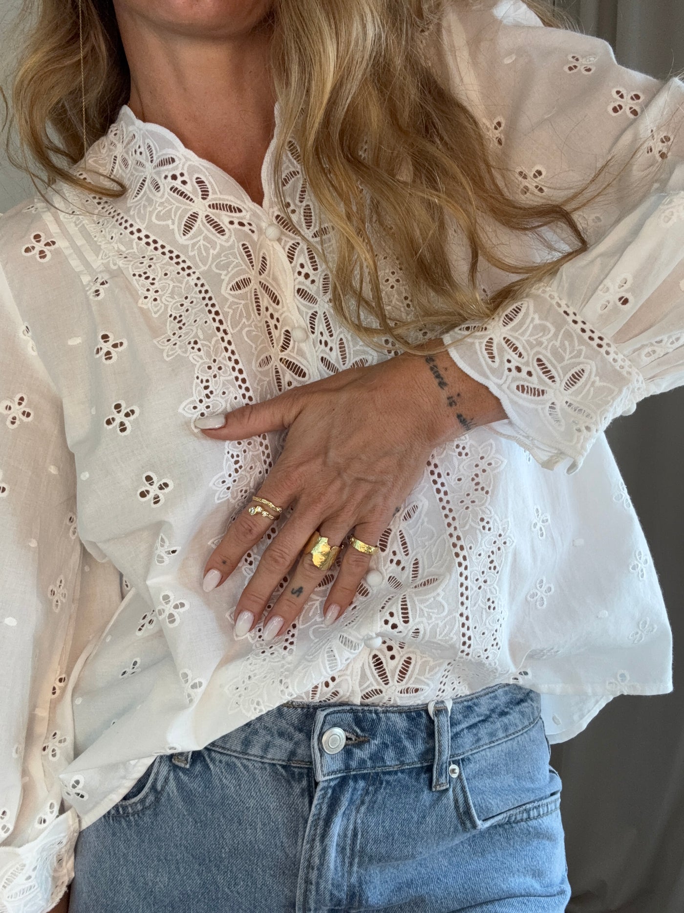 Hvid skjorte med broderi anglaise og blomsterdesign, knapper og pufærmer, bæres med blå jeans.