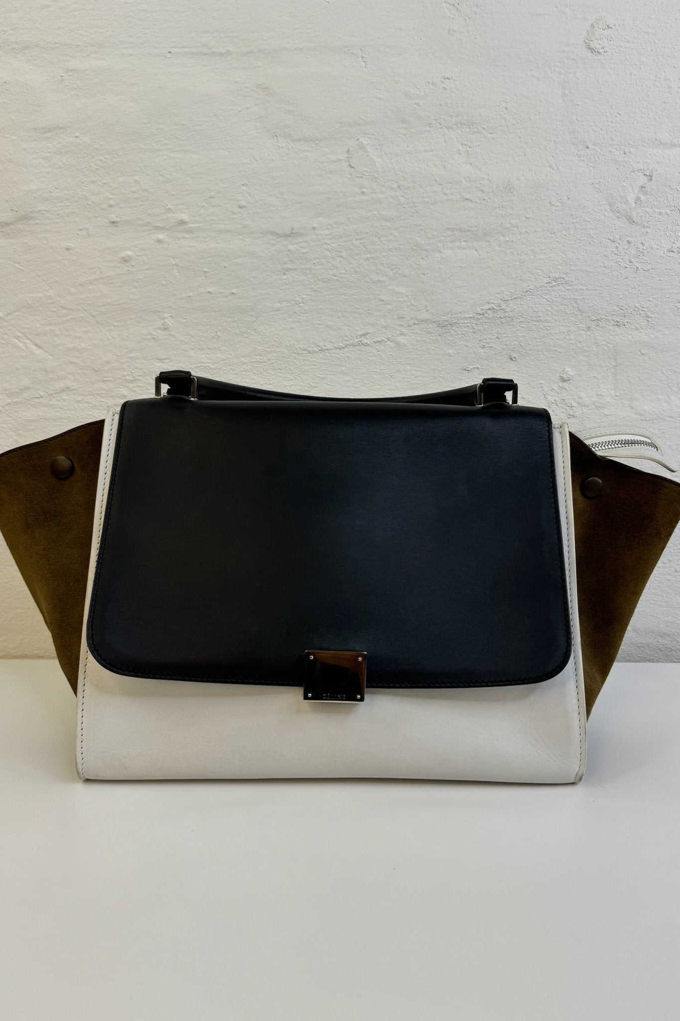 Sort/hvid Celine Trapeze taske med udvidede sider og klaplukning, mod en neutral baggrund.