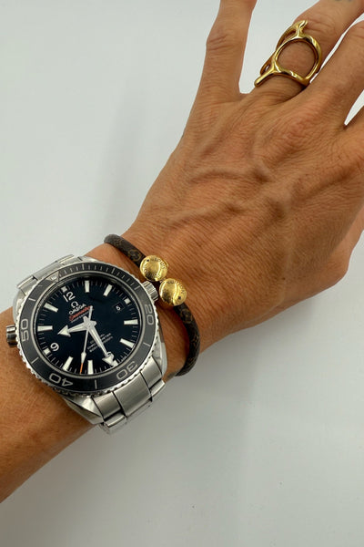 Hånd med Louis Vuitton armbånd, guldender med logo, og et ur. Armbåndet har et klassisk mønster.