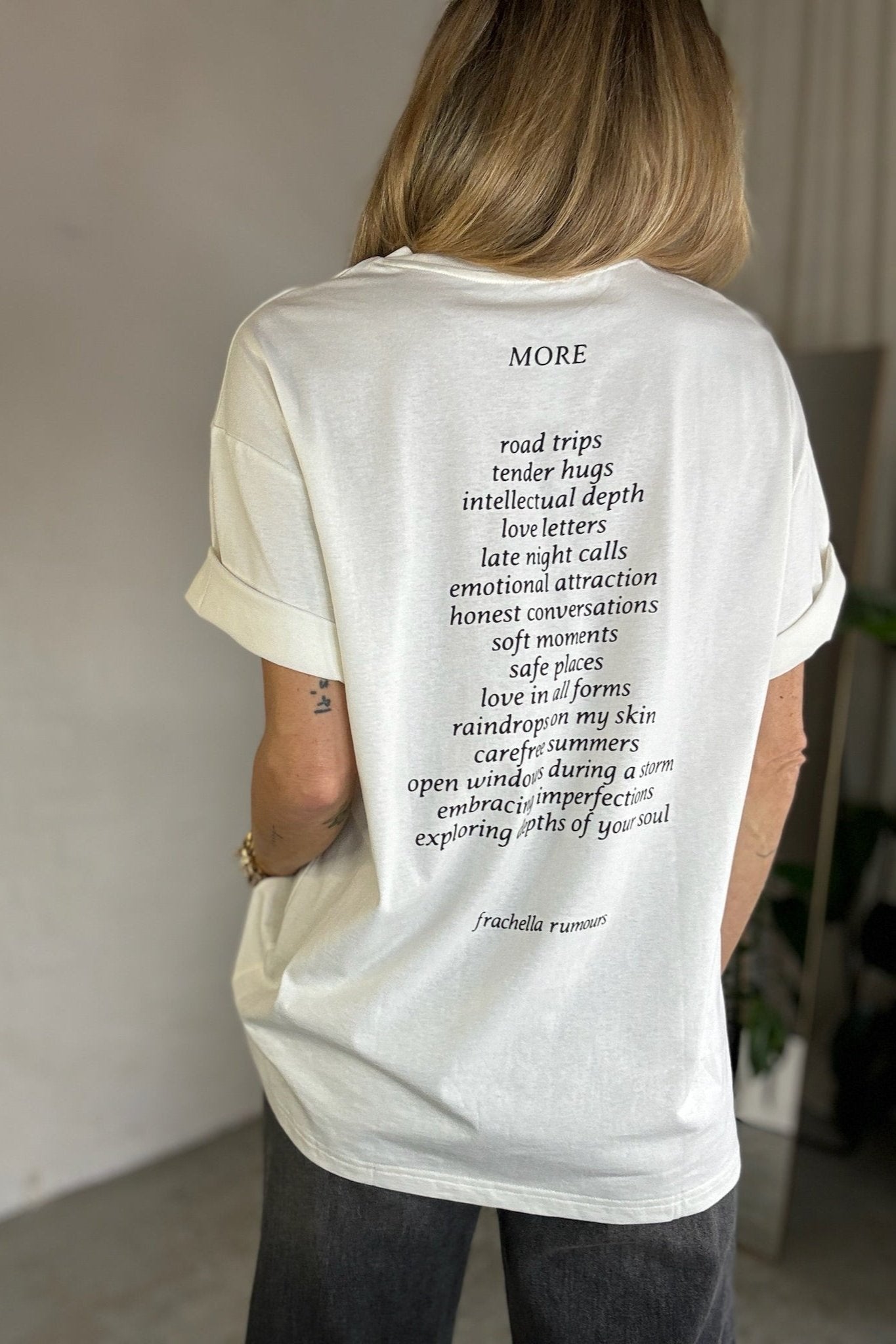 Person bagfra med hvid t-shirt, tekst trykt på ryggen med ord som "road trips" og "tender hugs".