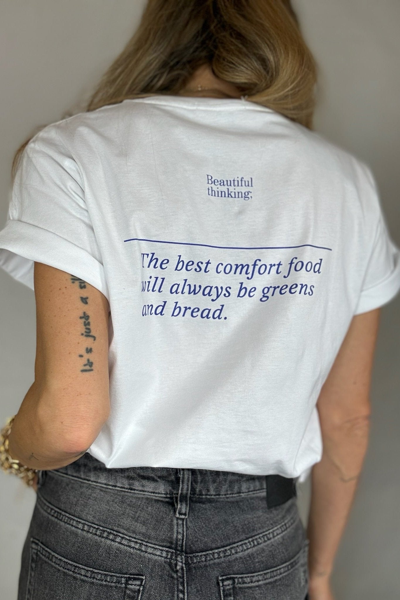 Person i hvid t-shirt med blå tekst: "Beautiful thinking; The best comfort food will always be greens and bread."